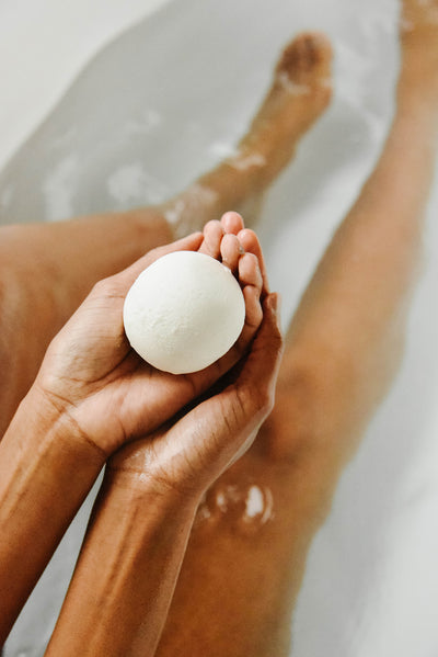 an all natural bath bomb held in a woman's hands over a bathtub