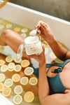 a bath full of citrus with a woman scooping out yamon's all natural bath crystals or bath salts