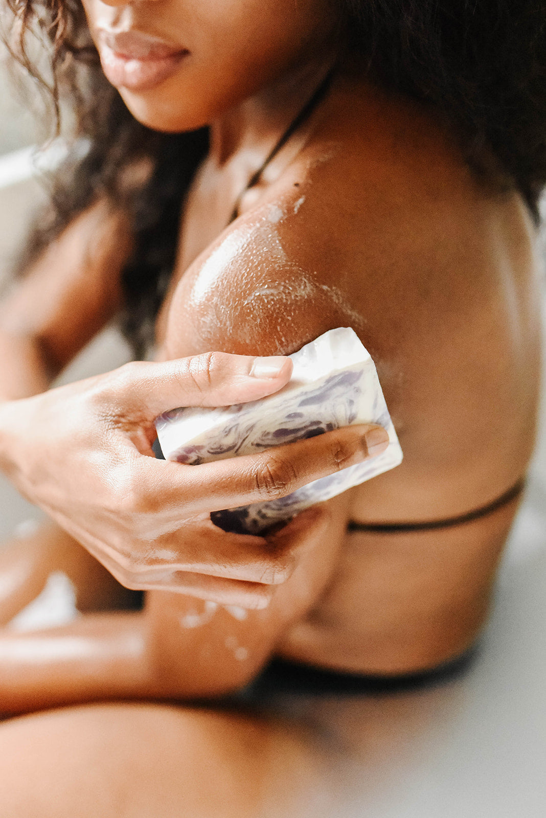 woman using an all natural soap bar to wash her shoulders in a bathtub